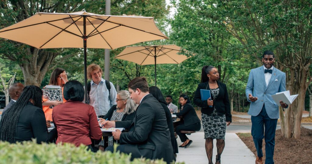 Students sitting at outdoor patio tables while prospective students are touring the grounds.